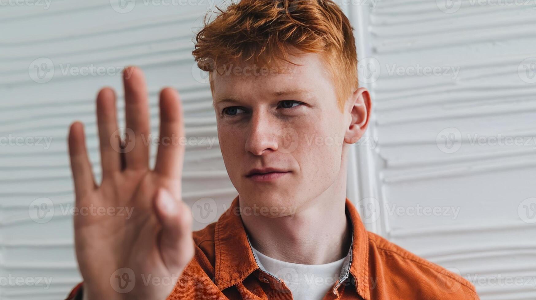 A young man with red hair making a stop sign photo