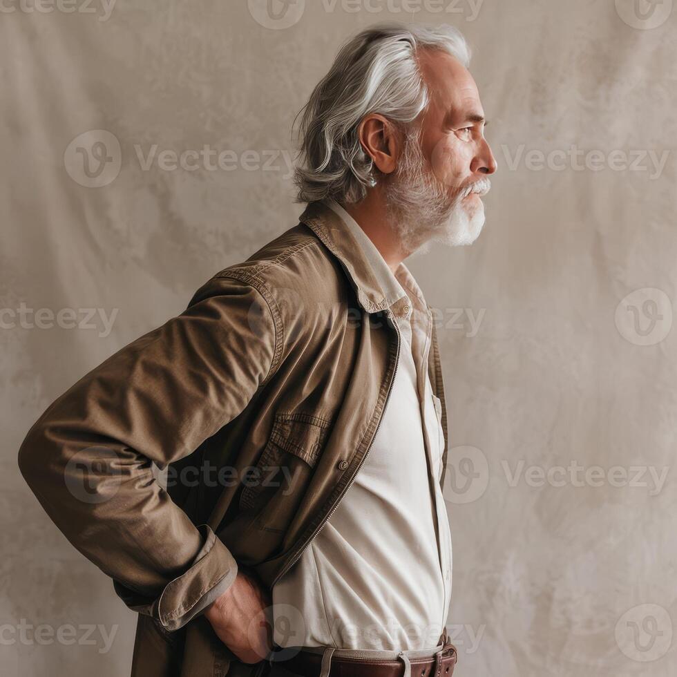 A man with a white beard and a white shirt is standing in front of a wall photo
