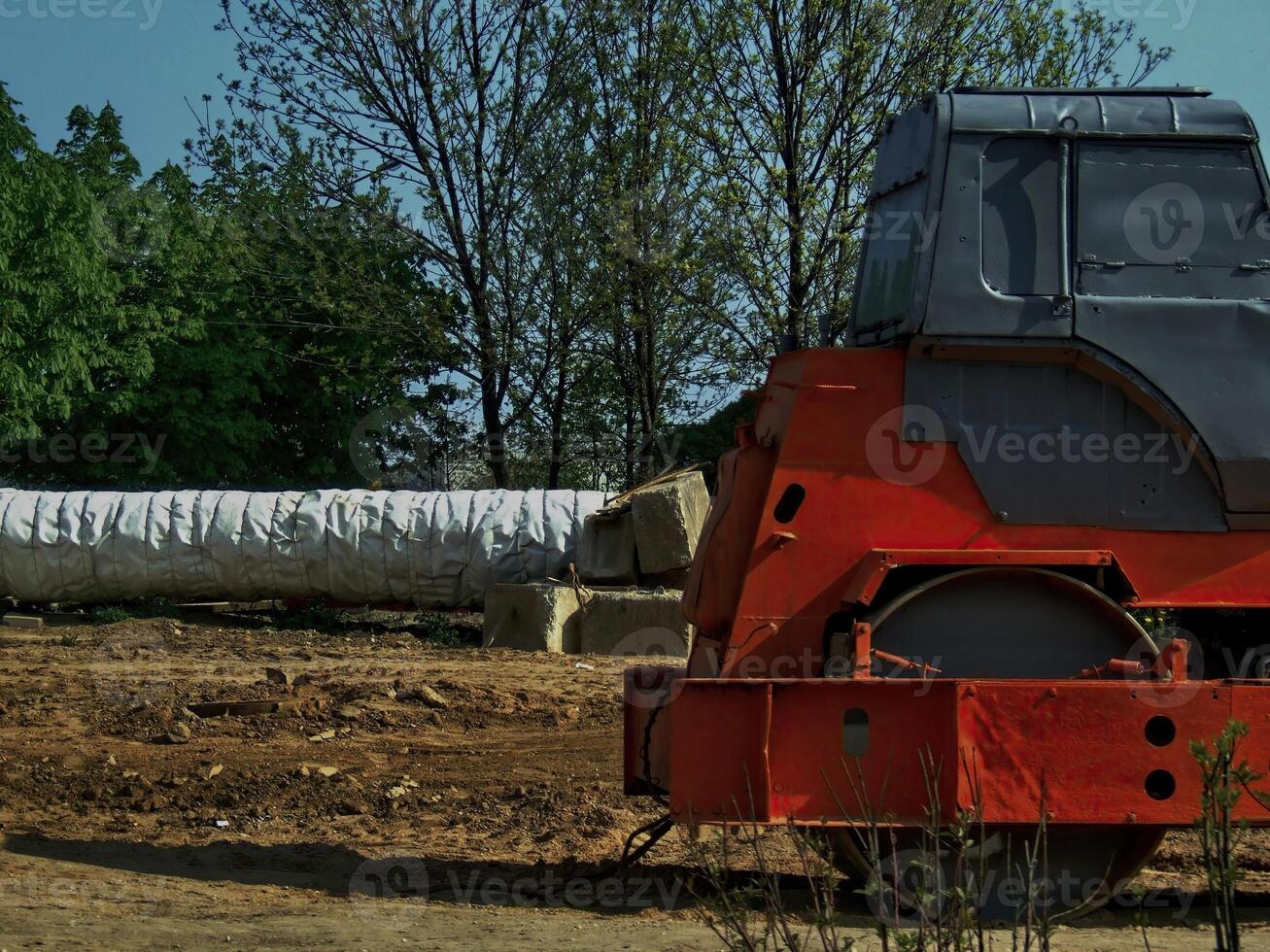 Heavy machinery compacts soil at a construction site during a sunny afternoon photo
