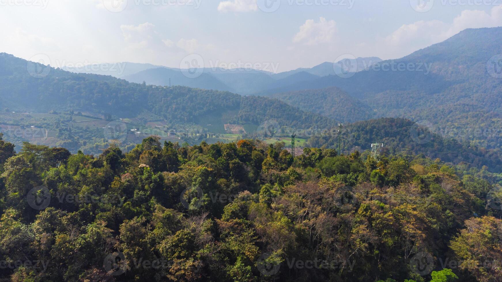 Lush green forest covering mountain range in Thailand under hazy blue sky photo
