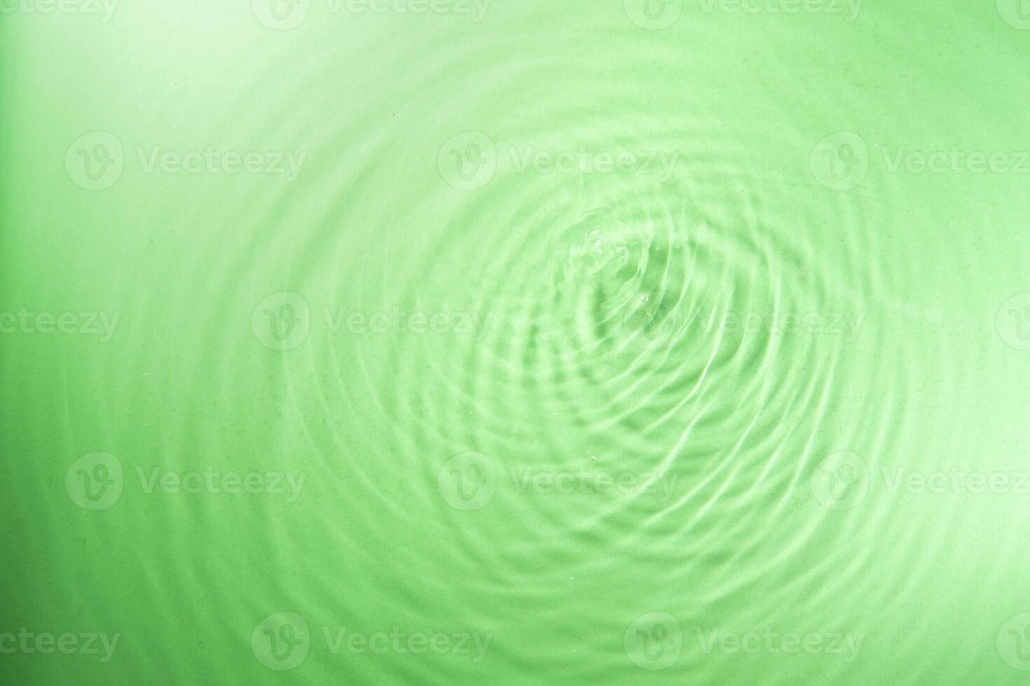 water droplet waves expanding on the water surface illuminated with green light photo