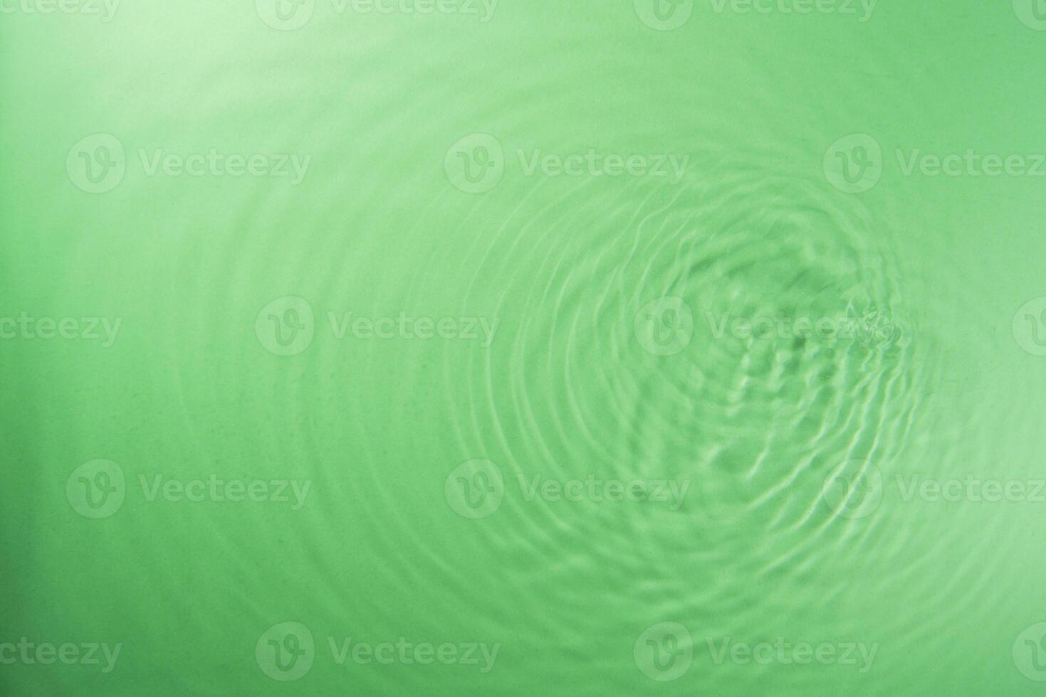 Concentric waves of green water droplets spreading over the surface of the water illuminated with green light photo