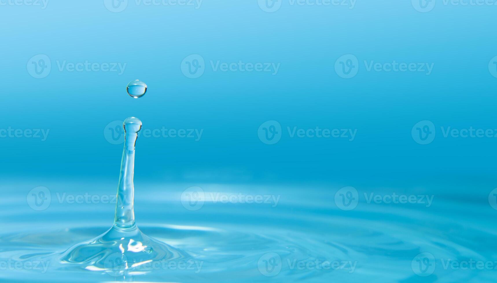 Water drops splashing on water surface forming waves against blue background photo