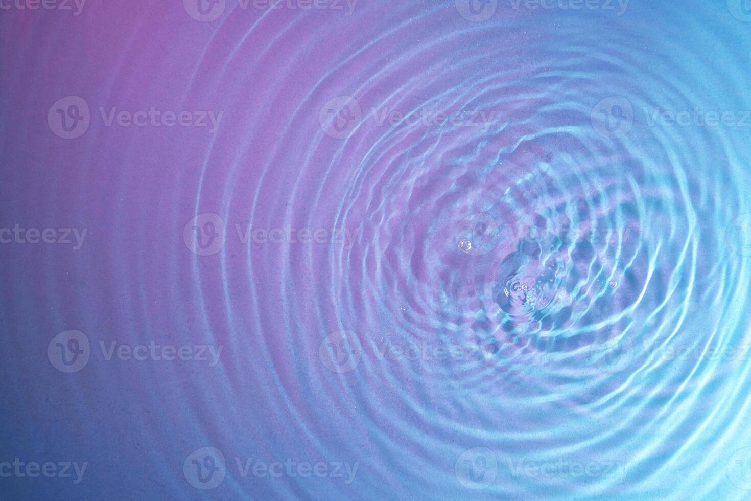 water droplet waves expanding on the water surface illuminated with blue and magenta light photo