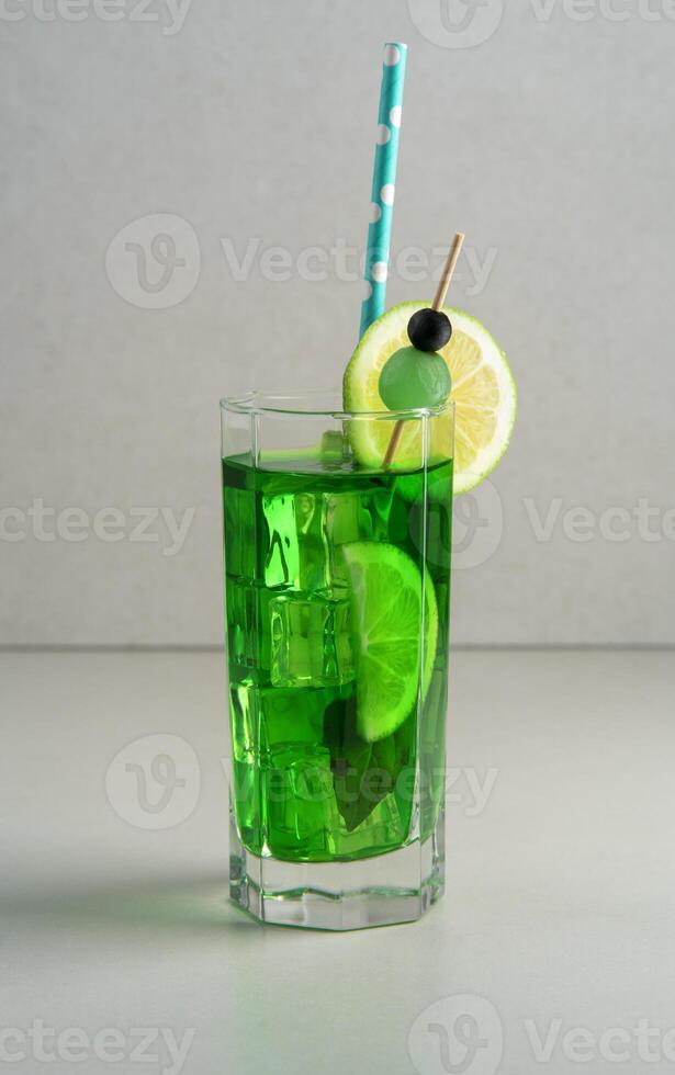 Front view of mint cocktail garnished with lemon slice, blue sherbet and green cherry on white table photo