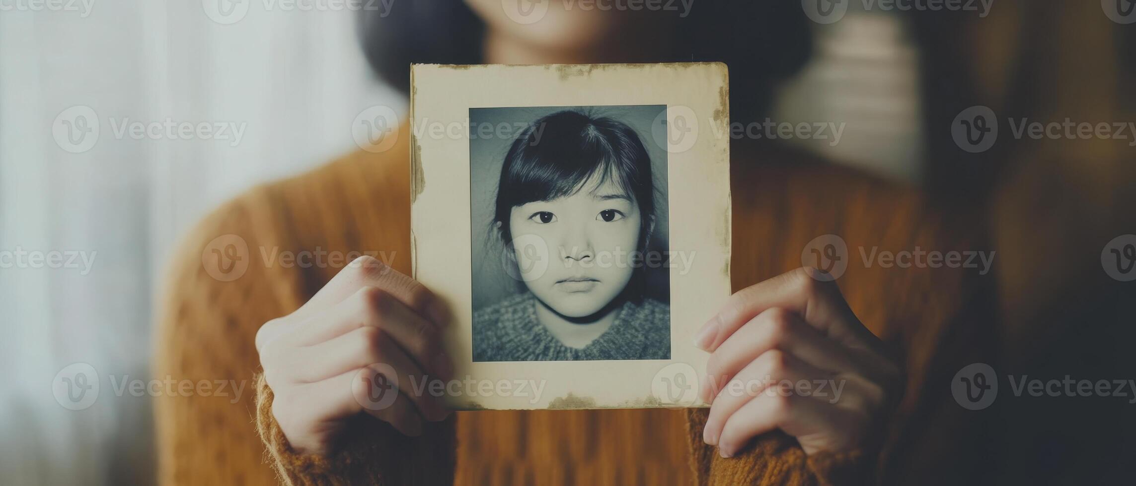 A person holds a vintage photograph of a child, evoking nostalgia and introspection in a warm, softly lit environment. photo