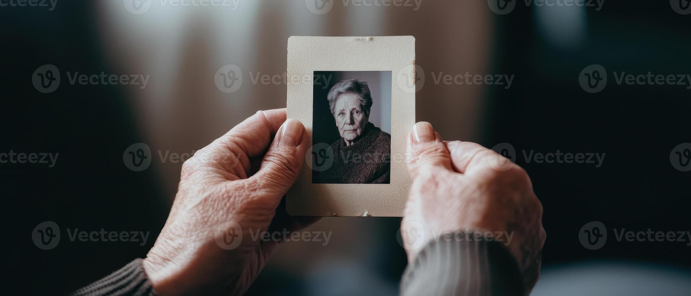 A pair of hands holding a vintage photo of an elderly woman, evoking nostalgia and memories in a softly lit environment.