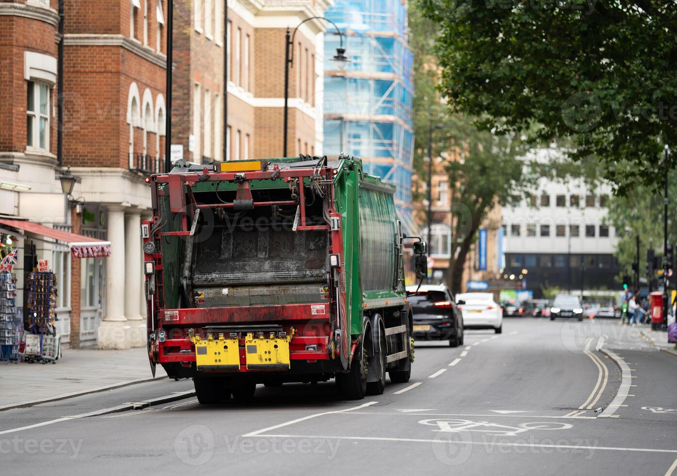 A green garbage truck navigates a London street, symbolizing the city dedication to sustainability amid a backdrop of classic British architecture.. photo