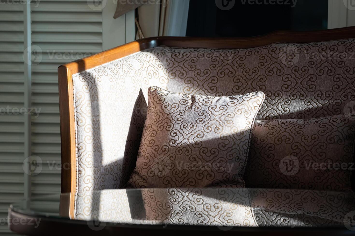 Sunlight shines on the elegant wooden sofa upholster ed with ivory velvet fabric and a round coffee table set in a living room. photo
