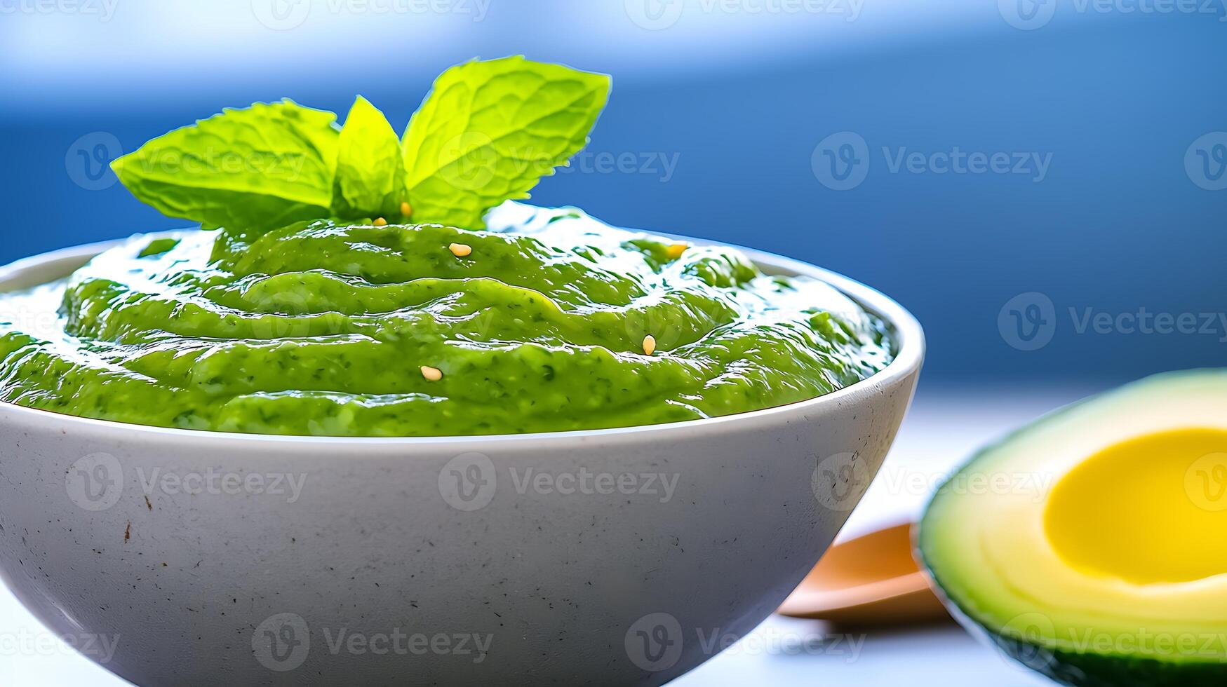 Fresh green avocado dip in a bowl garnished with mint leaves, with an avocado half beside it photo