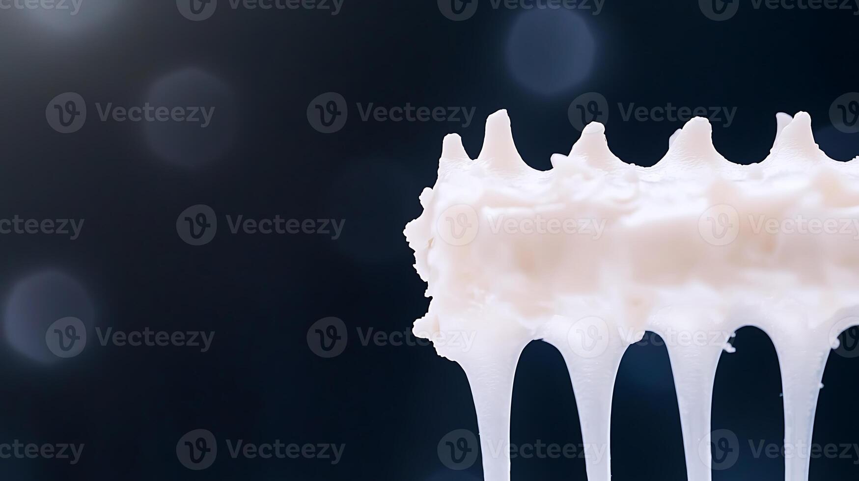 Close-up of whipped cream dripping from a whisk against a blurred dark background photo