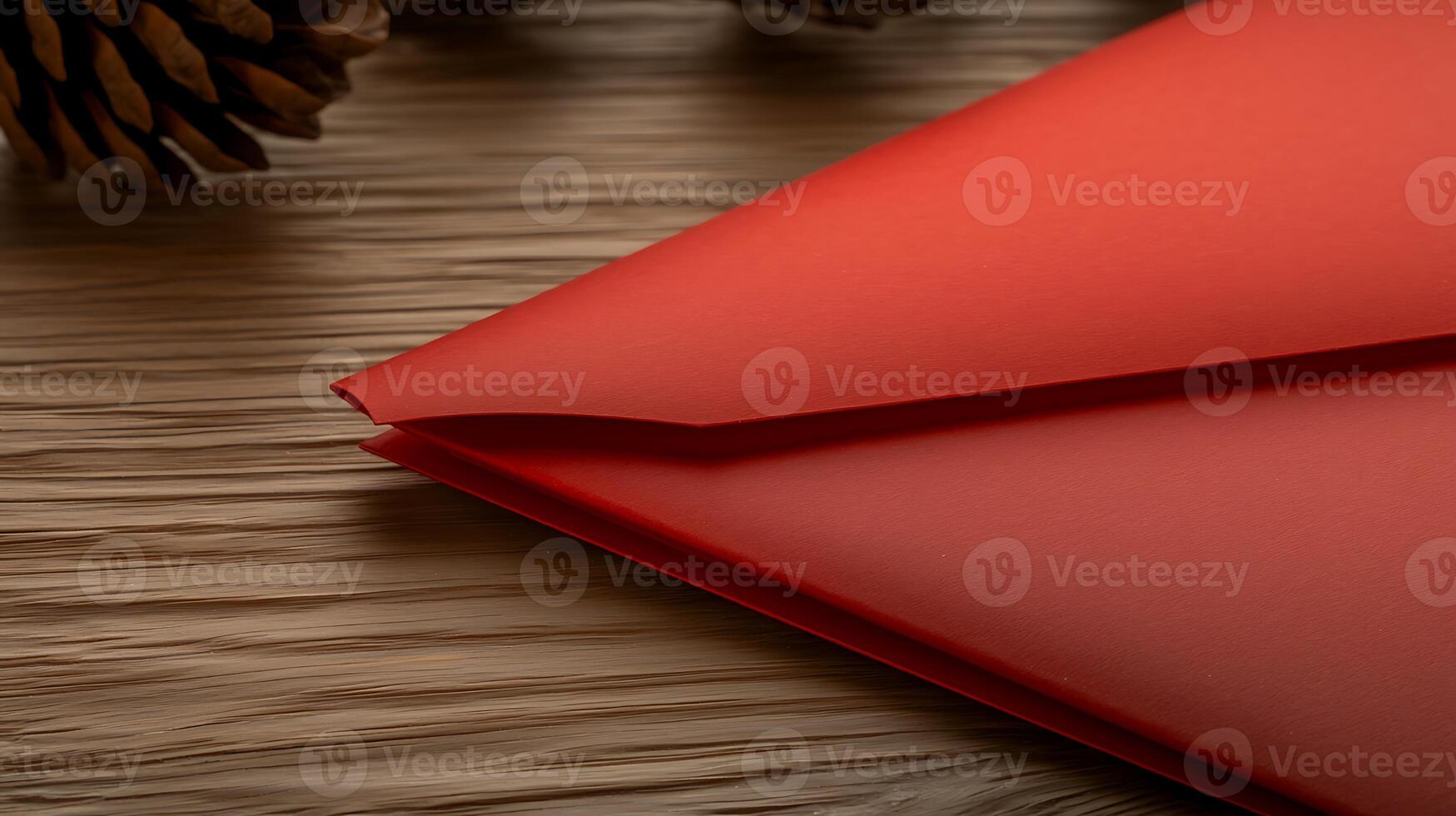 Red envelope resting on wooden surface with pine cones in the background, ideal for festive occasions photo
