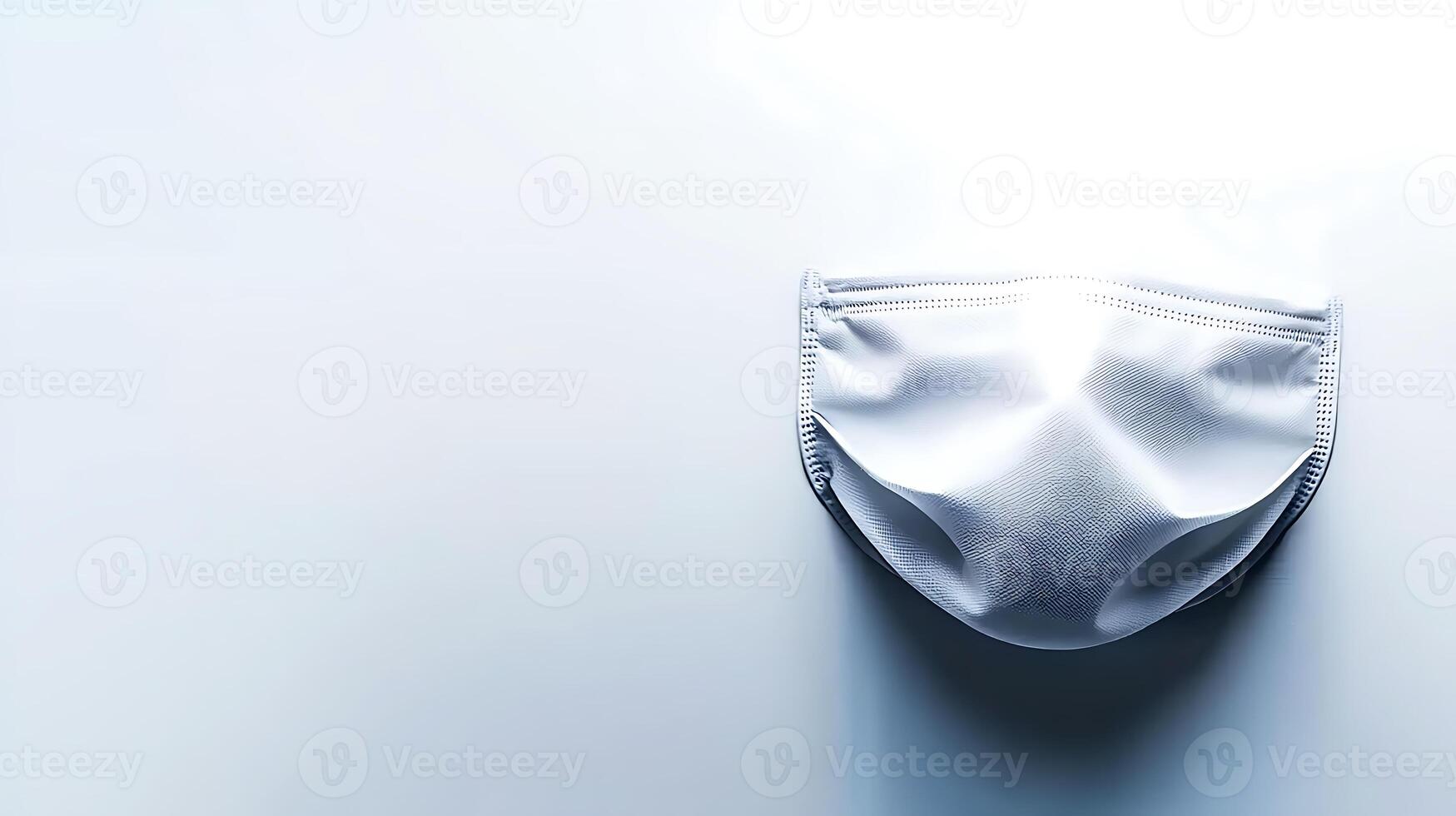A close-up view of a white face mask resting on a smooth surface, illuminated softly photo