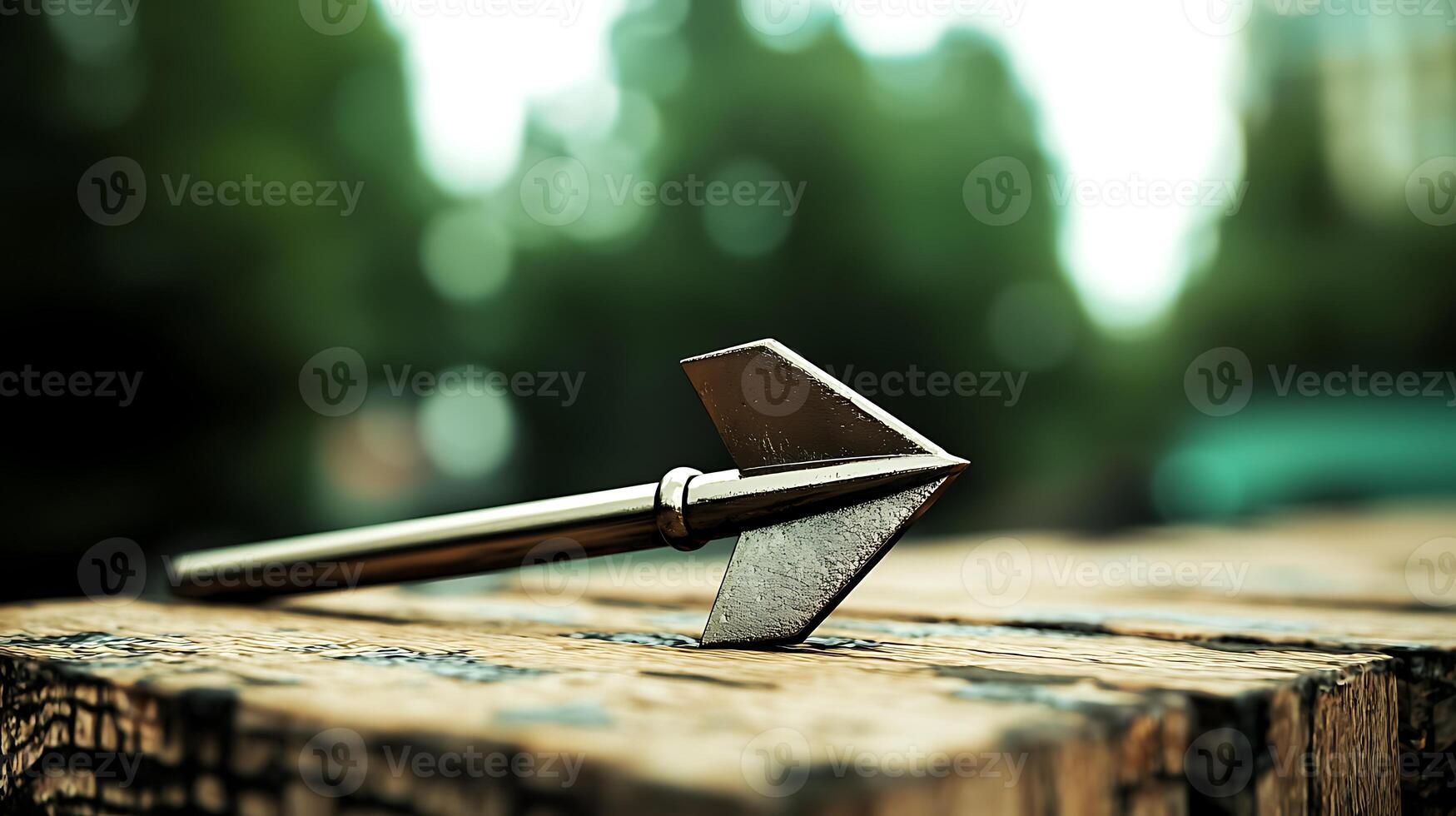 A close-up of a metallic arrowhead resting on a wooden surface in a lush green outdoor setting photo