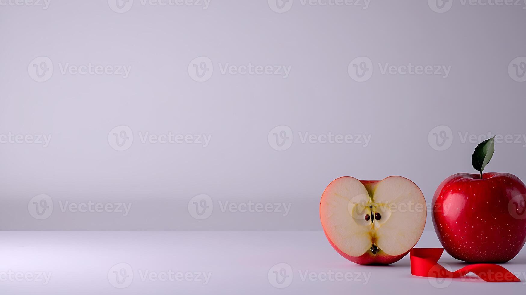 A fresh red apple and a sliced half on a clean white surface with a red ribbon nearby photo