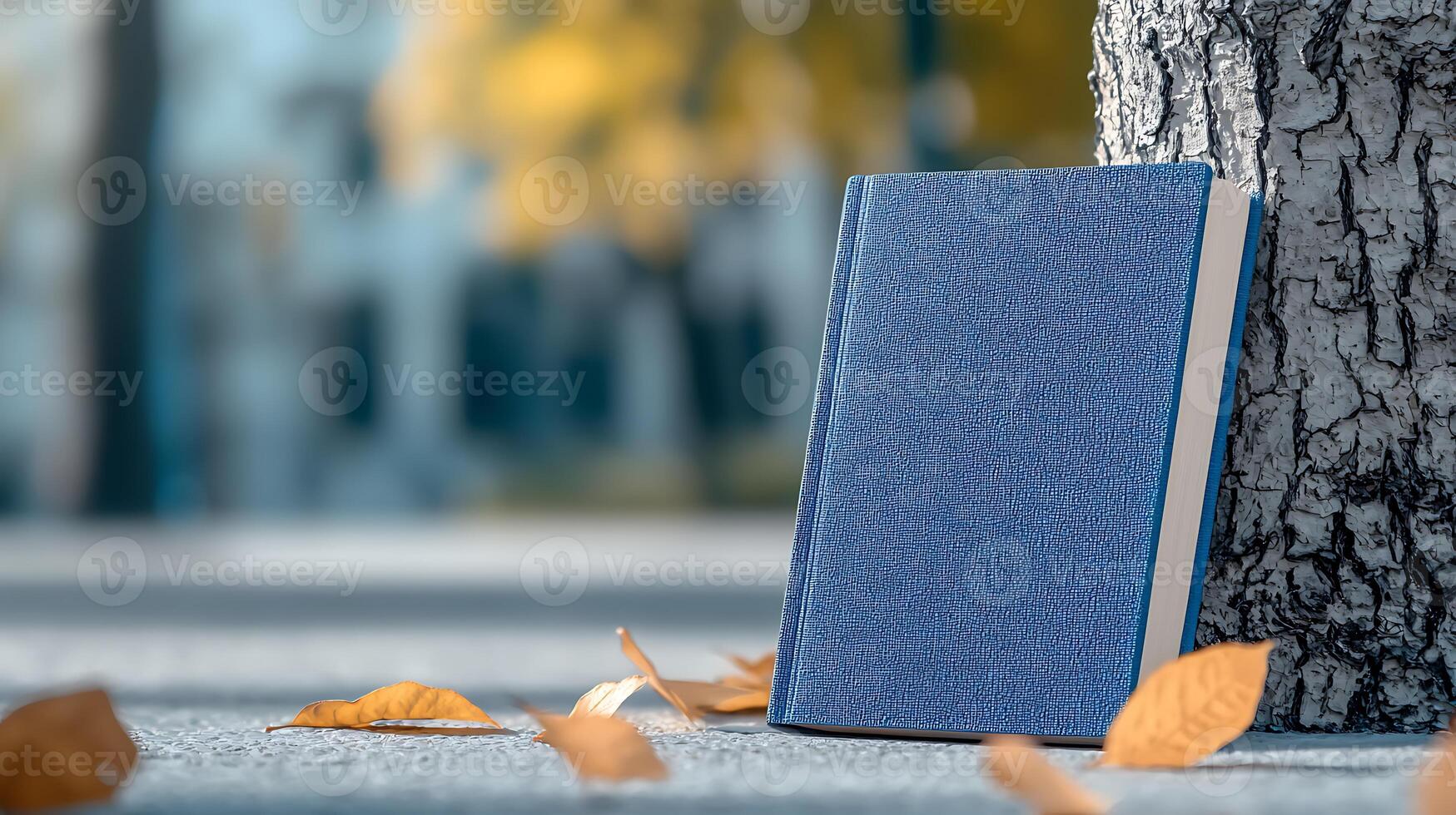 A serene autumn scene featuring a blue book resting against a tree trunk with fallen leaves photo