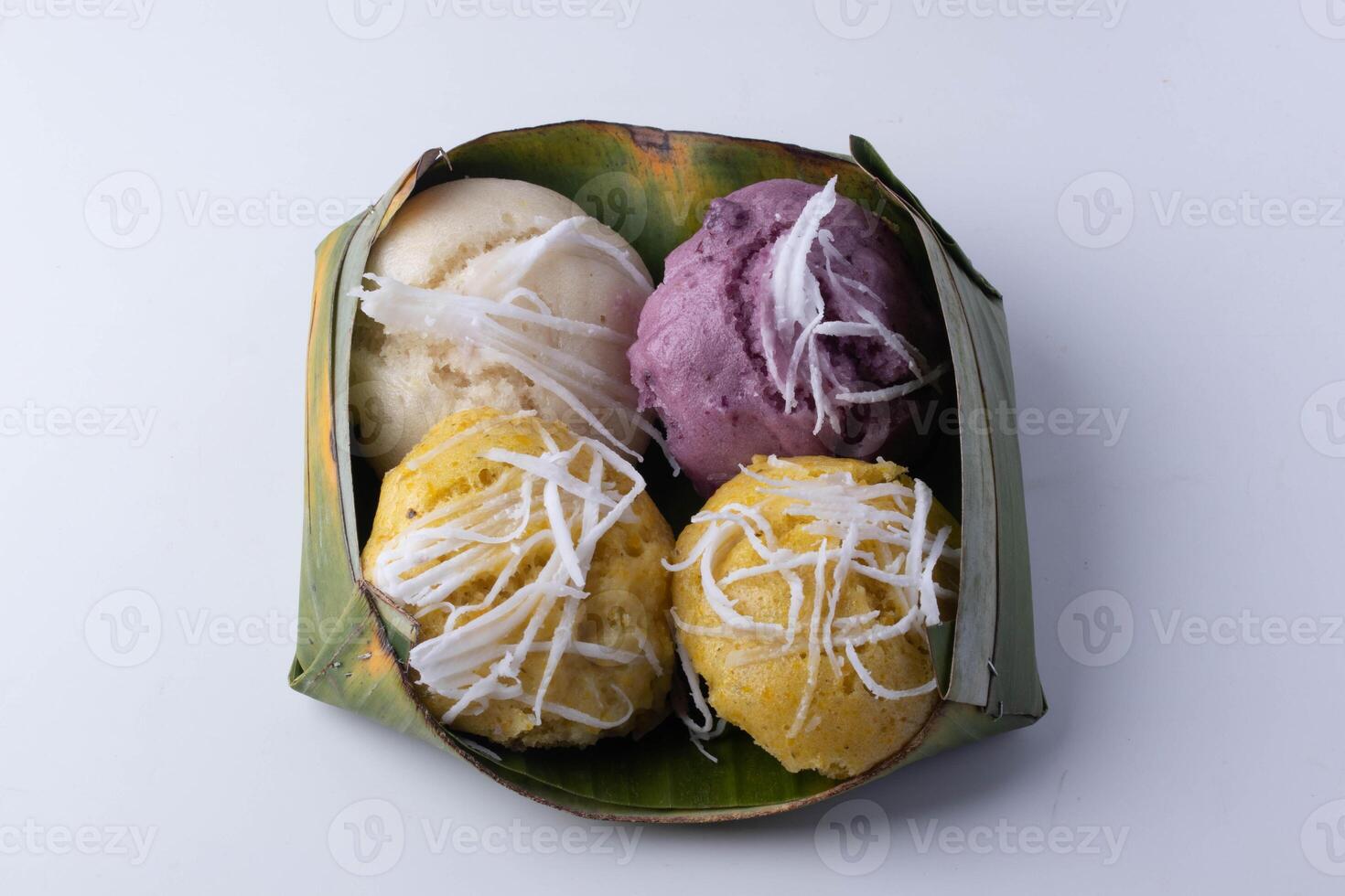 variety of colorful steamed rice cakes topped with shredded coconut are presented in banana leaf container, showcasing traditional Asian dessert photo