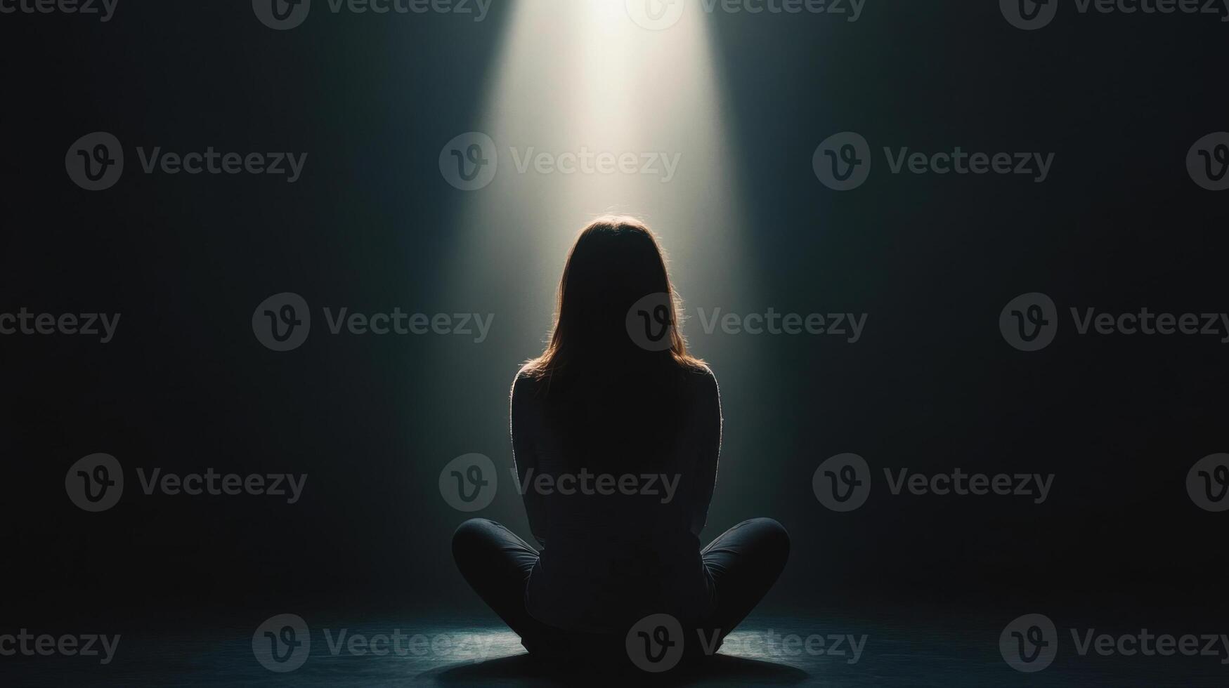 woman sits alone in dark room, illuminated by single beam of light, creating contemplative and serene atmosphere photo