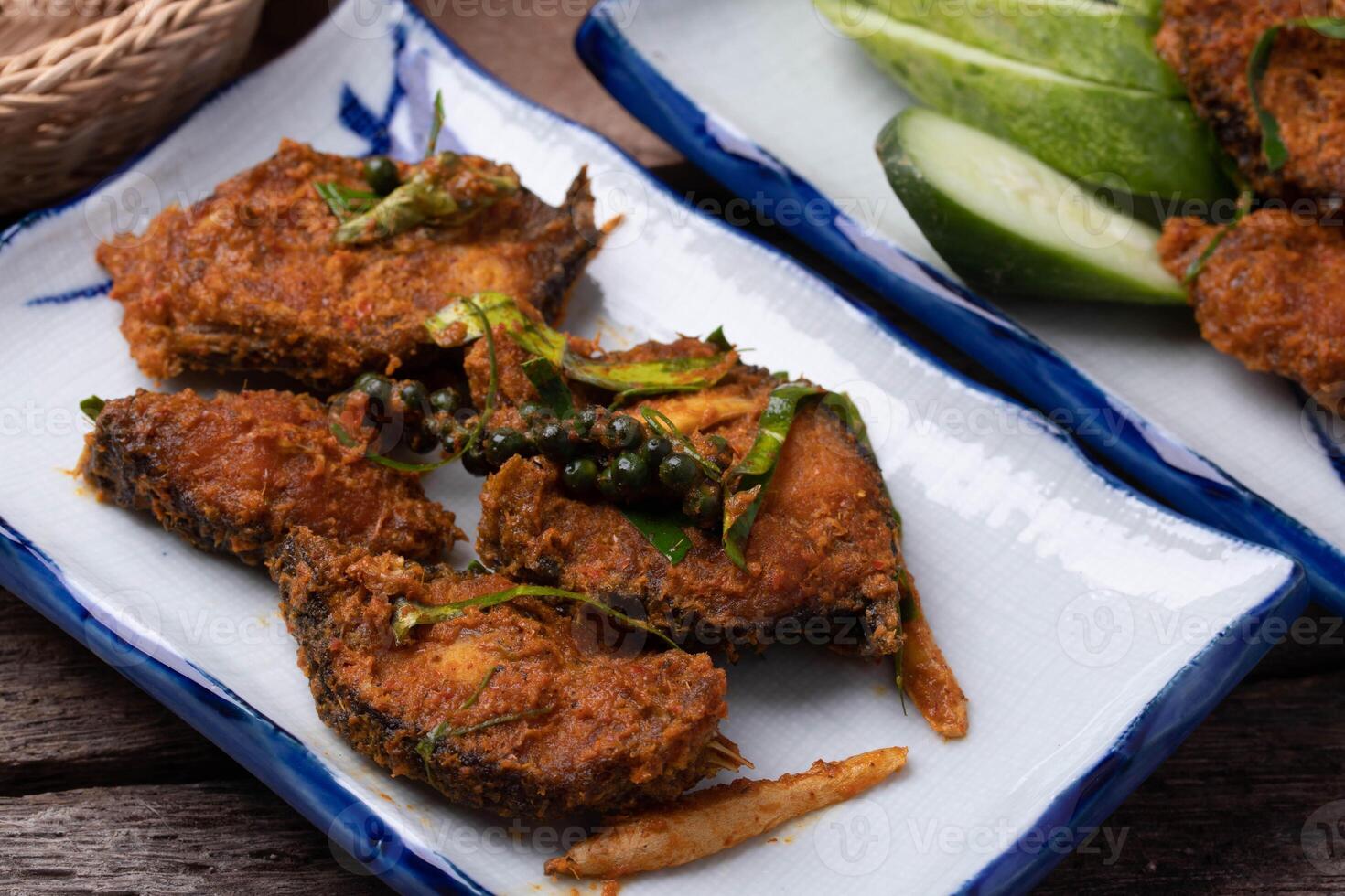 Spicy fried fish with herbs served on ceramic plate, accompanied by fresh cucumber slices, showcasing vibrant and appetizing presentation photo
