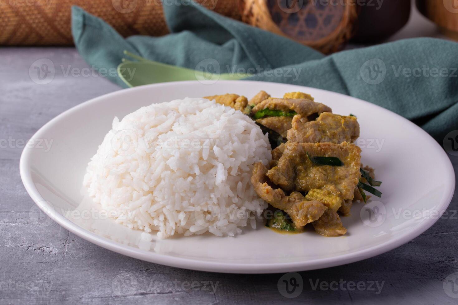 plate of white rice served with stir fried meat and vegetables, garnished with green herbs, is set on table with green cloth and decorative background elements photo