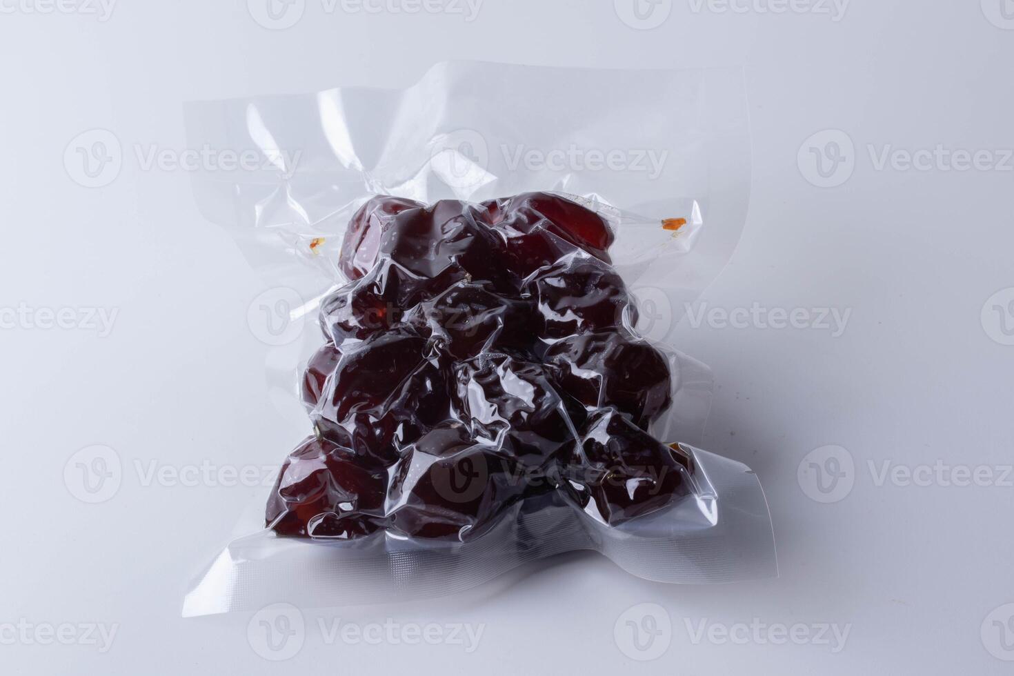 vacuum sealed package of dark red dates on white background. packaging is clear, showcasing glossy texture of dates inside photo