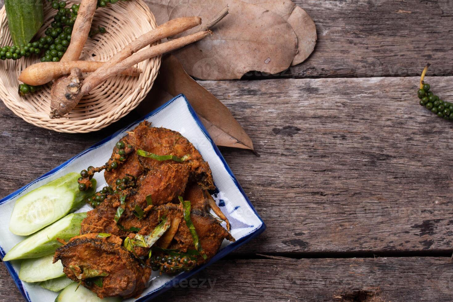 plate of spicy fried crab garnished with fresh herbs and served with cucumber slices on rustic wooden table, accompanied by basket of fresh ingredients photo