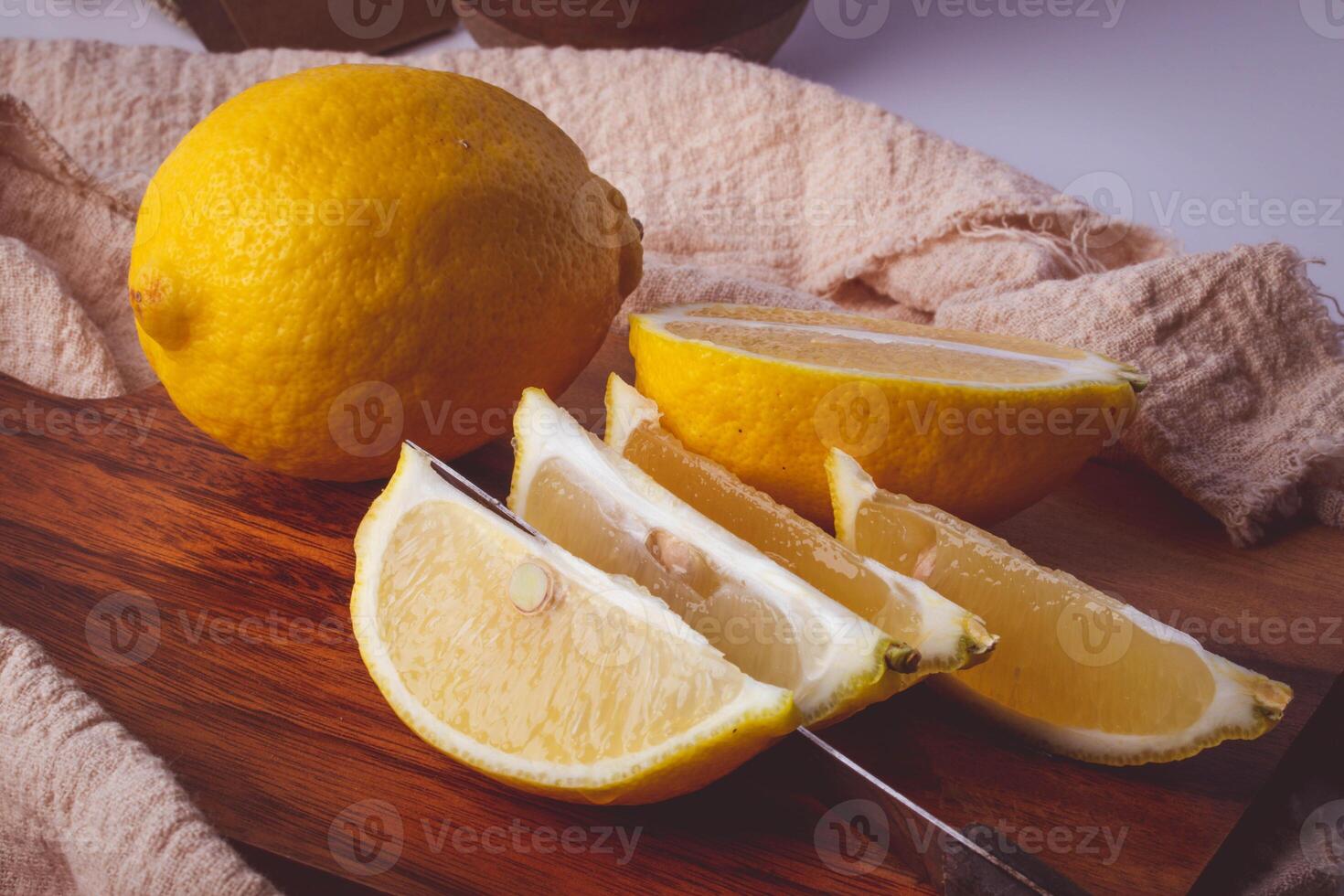 whole lemon and sliced lemon wedges on wooden cutting board with knife, set against textured cloth background photo