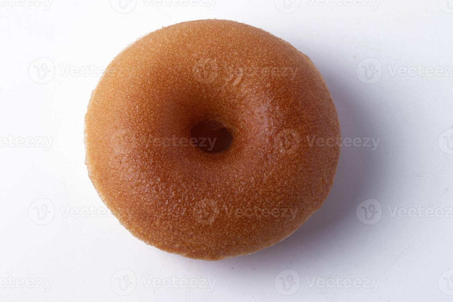 plain, glazed donut sits on white background, showcasing its smooth texture and classic round shape. donut golden brown color highlights its freshly baked appearance photo