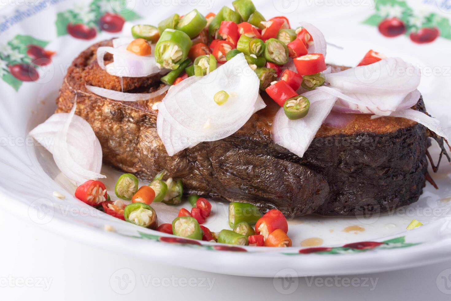 plate of fried fish topped with sliced onions and colorful chili peppers, showcasing vibrant and spicy dish. fish is crispy and golden brown, served on decorative plate with floral pattern photo