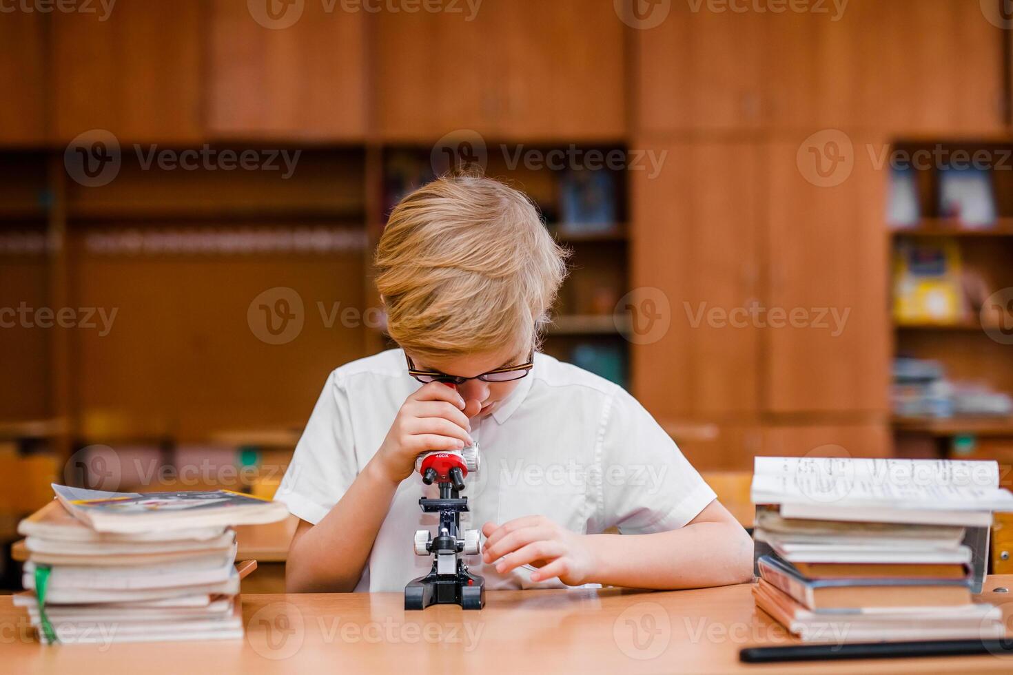 Boy with impairment in glasses carefully studying textbooks at a school desk photo