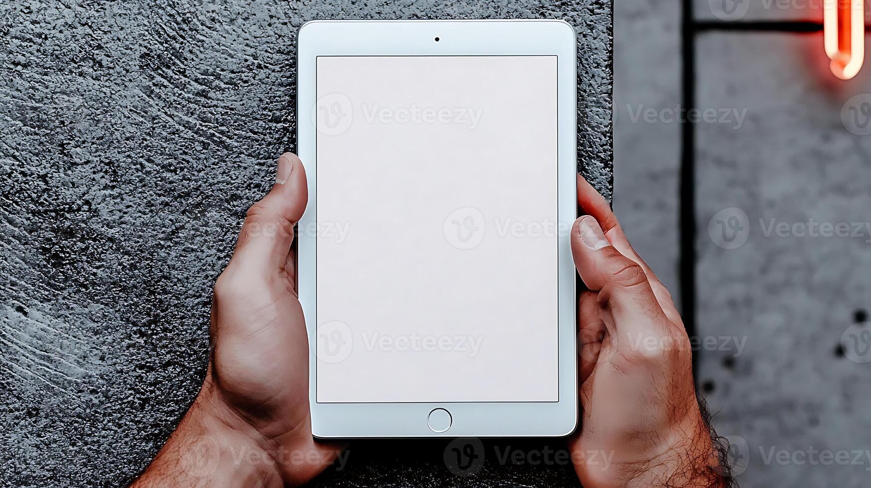 Person holding a blank tablet against a textured gray wall with soft lighting in the background photo
