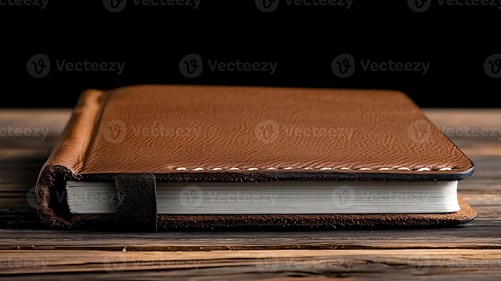 A close-up view of a brown leather notebook resting on a wooden table in a dimly lit setting photo