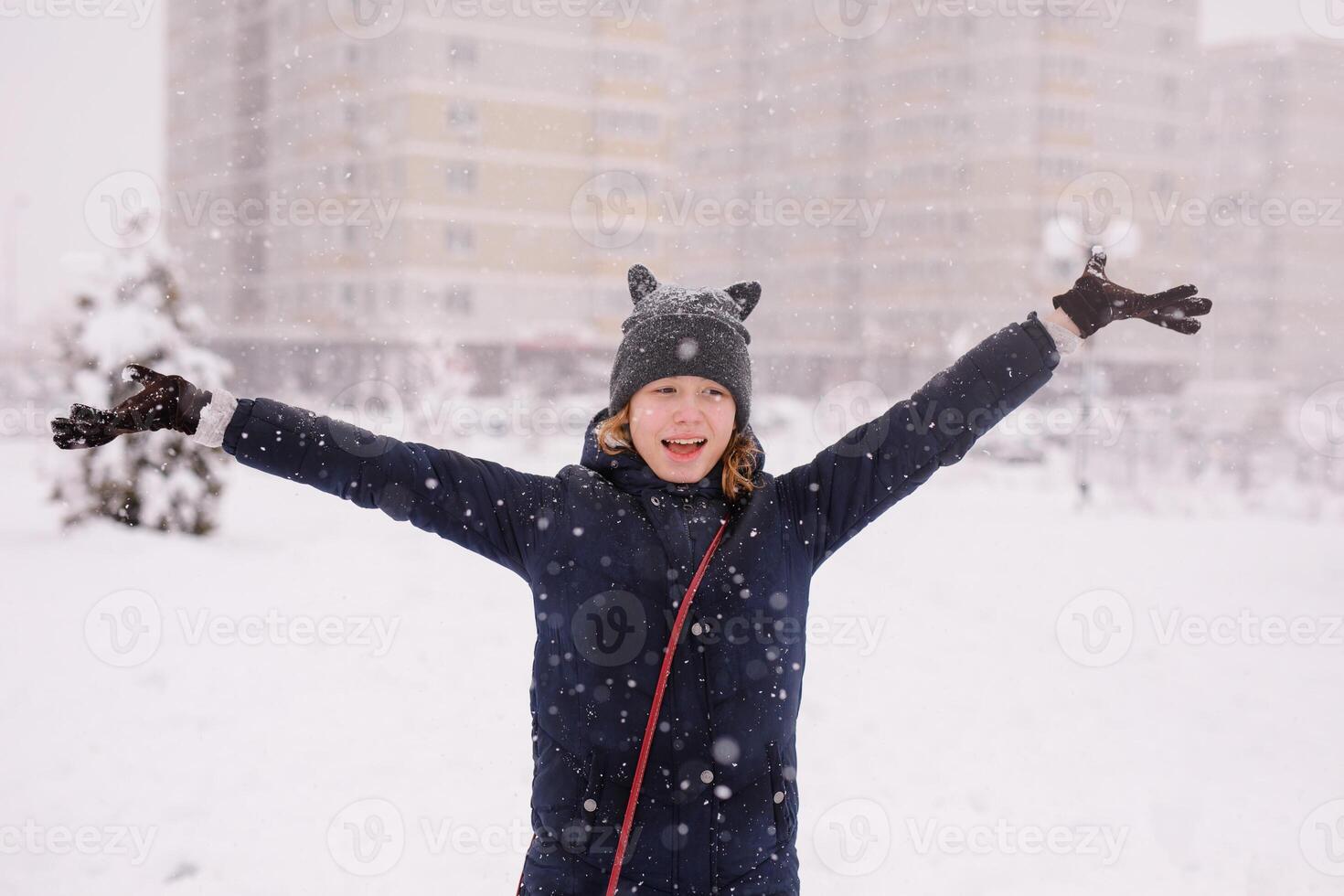 Portrait of happy 12 year-old girl in a warm jacket and a cat-ear hat under heavy snow photo