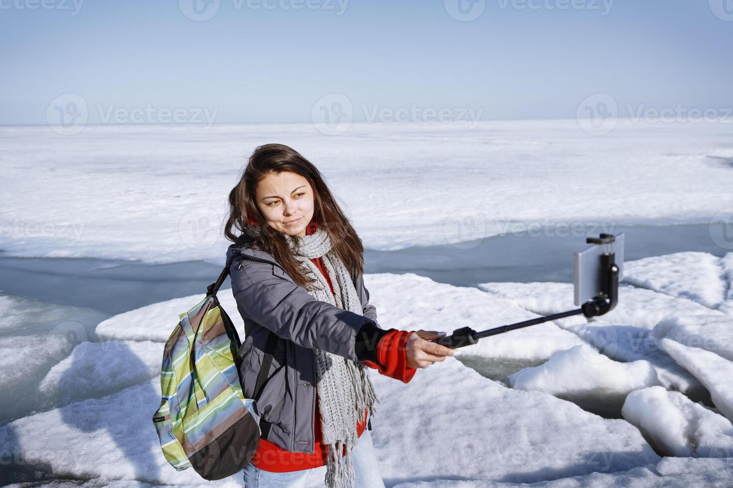 Female traveler at icy landscape using monopod to make photo