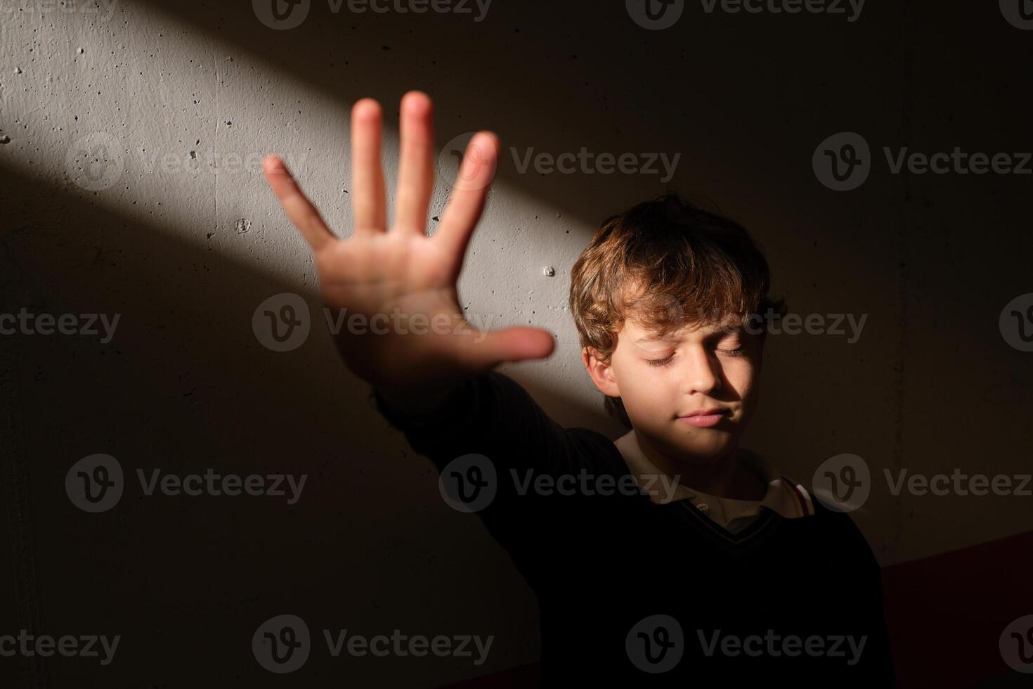Boy with closed eyes showing stop gesture to sudden sunbeam photo