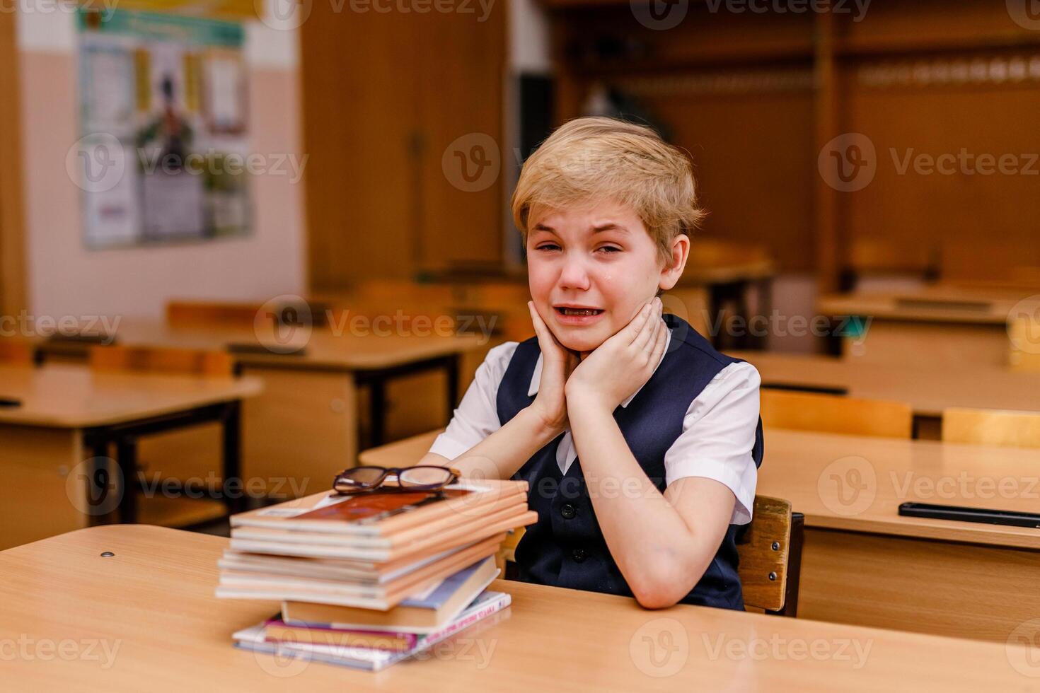 Little schoolboy crying at his desk in a classroom photo