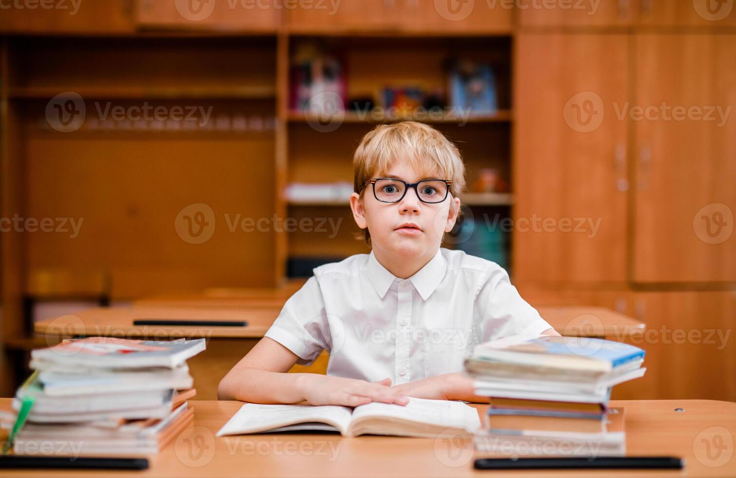 Student boy reading a book and looking very surprised in his school classroom photo
