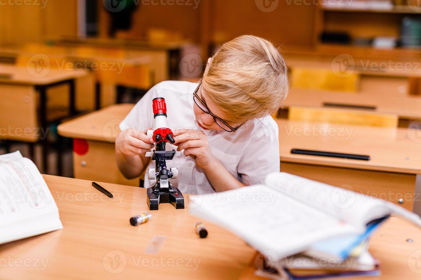 Boy with visual impairment in glasses carefully studying textbooks at school desk photo