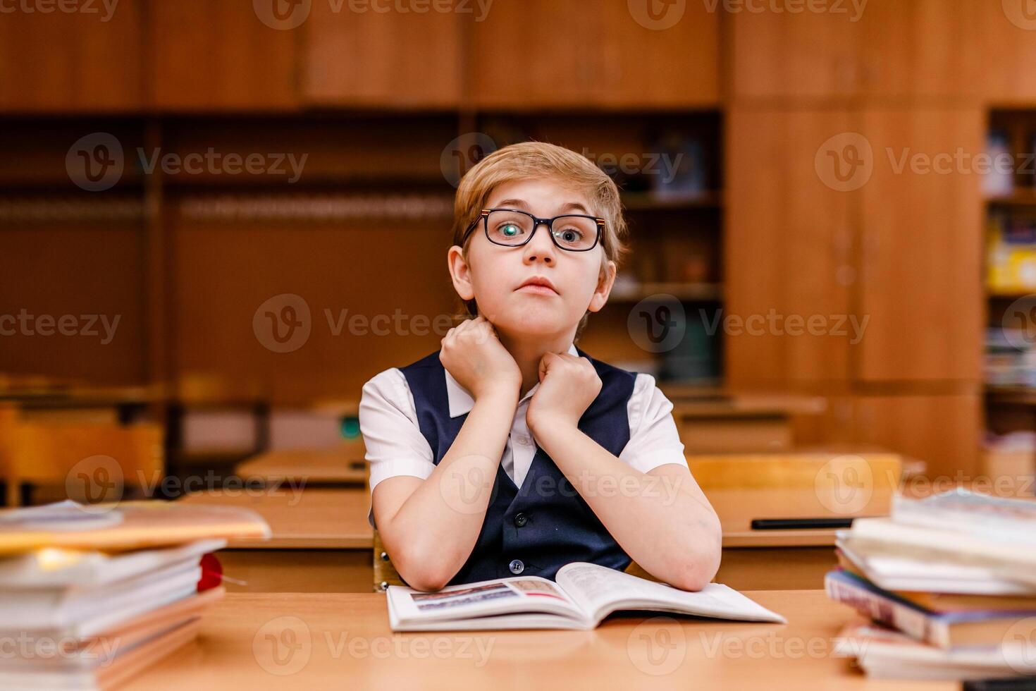 8-year-old schoolboy in glasses, white shirt, and vest studying and reading books in classroom photo