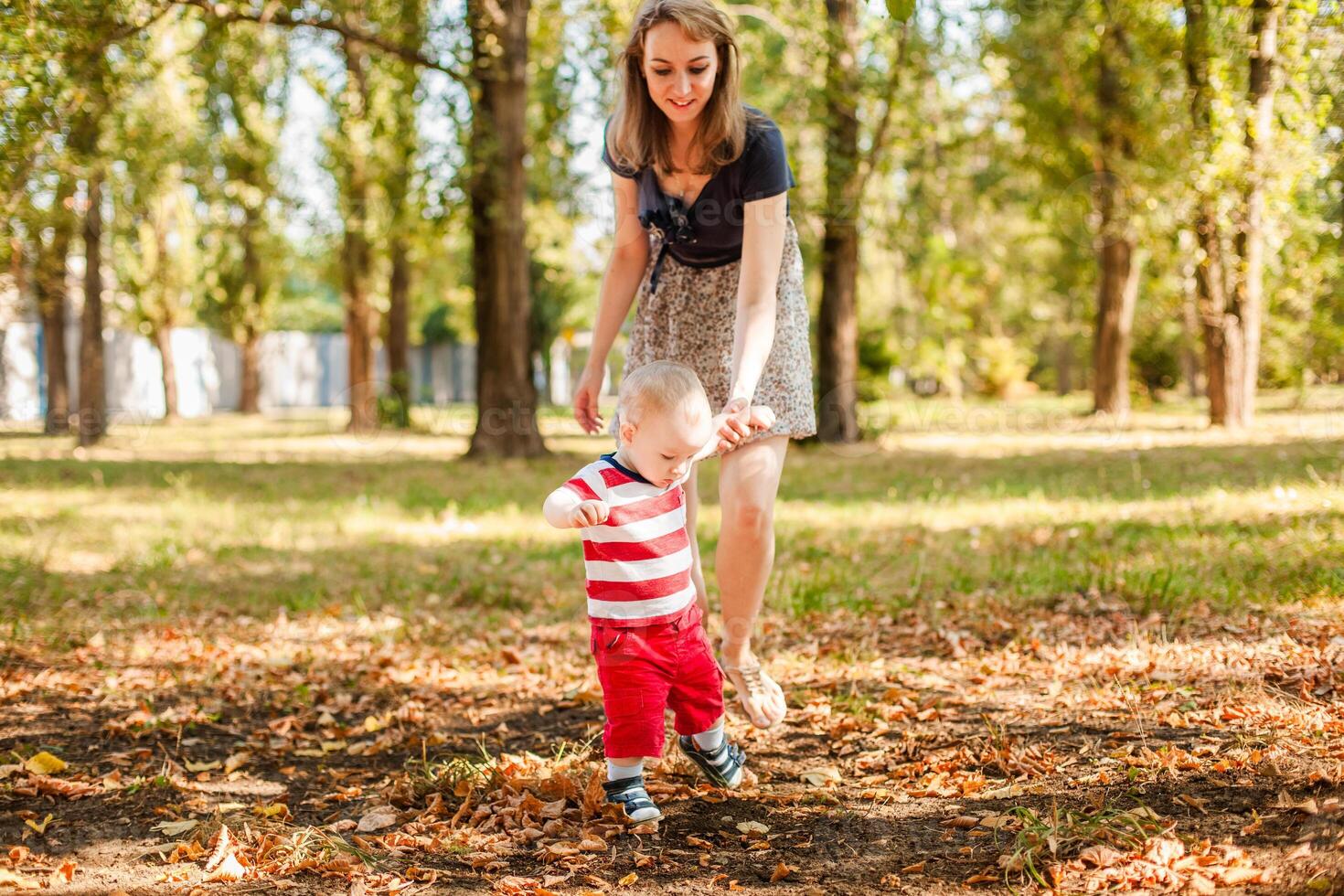One-year-old baby walking hand in hand with mom in a warm sunny park photo