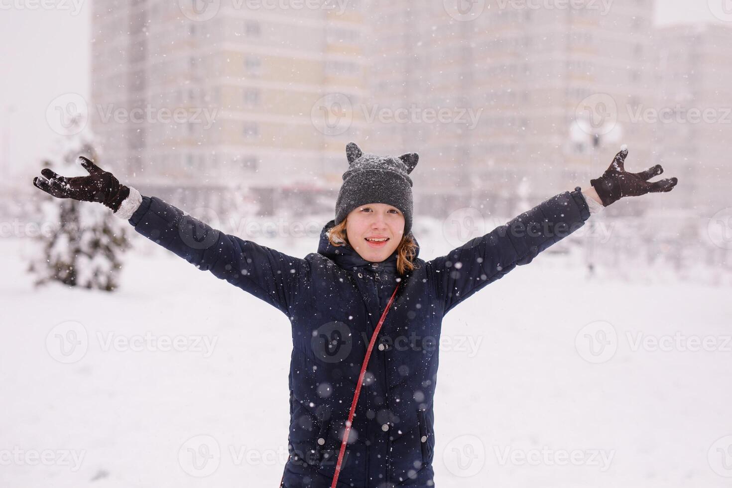 Portrait of an happy 12-year-old girl in a warm jacket and a cat-ear hat under heavy snow photo