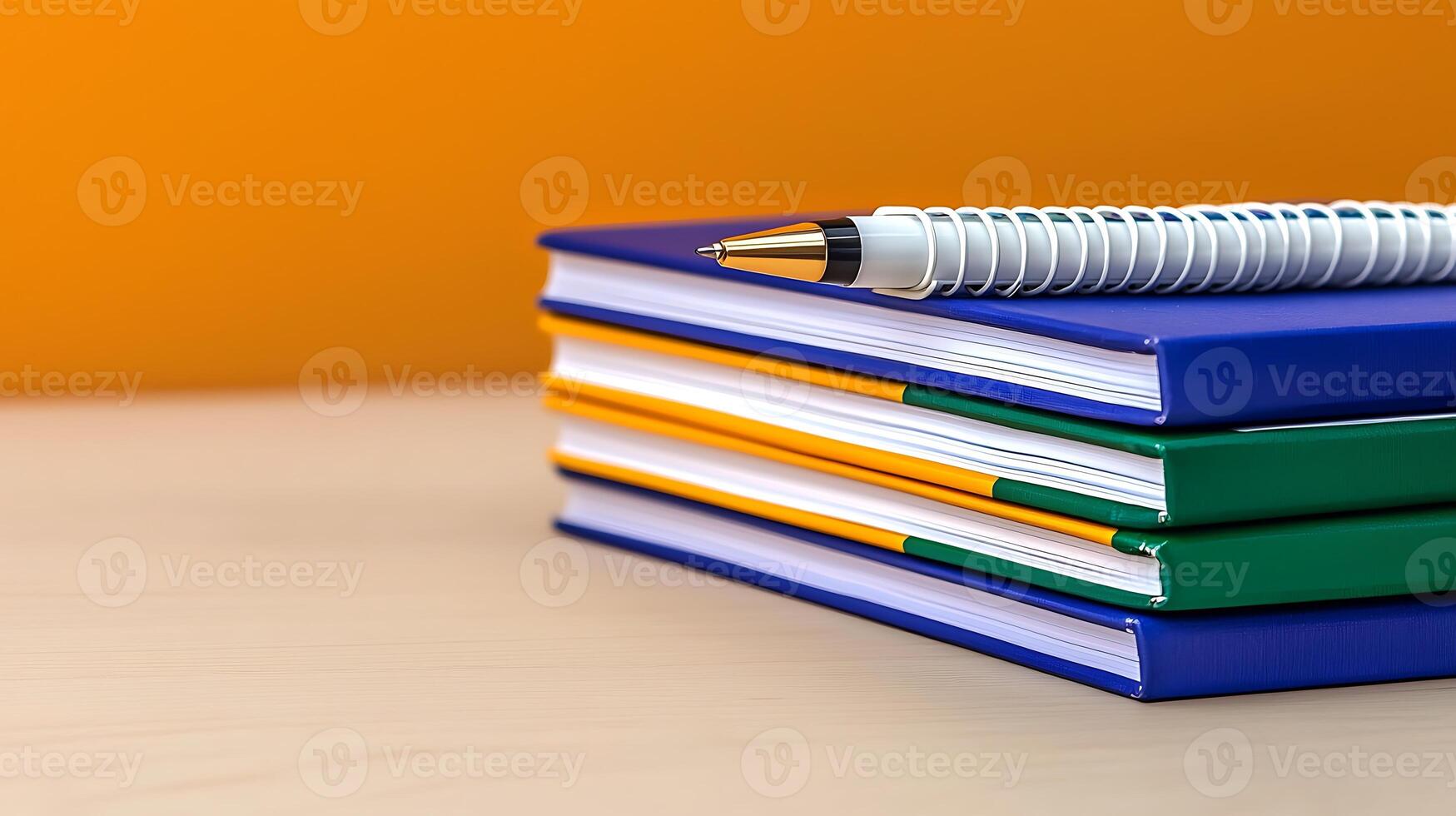 Stacked colorful notebooks and a pen on a desk with a vibrant orange background photo