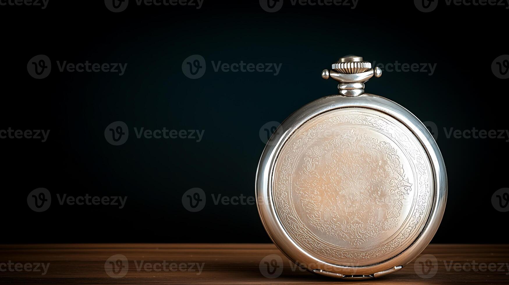 Vintage silver pocket watch resting on a wooden table with a dark background, showcasing intricate details photo