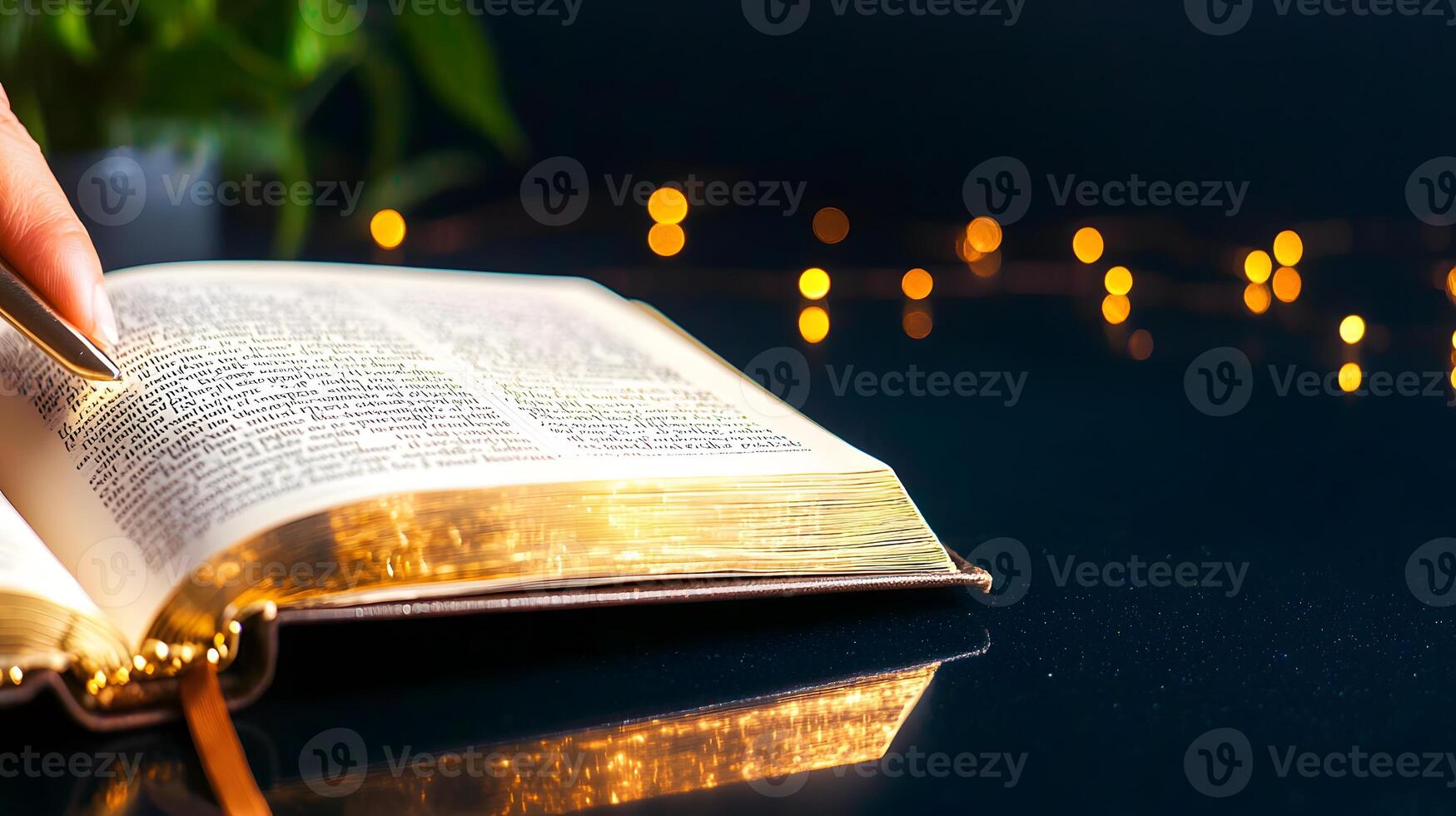 Open book with a hand turning the page, surrounded by soft glowing lights and greenery photo