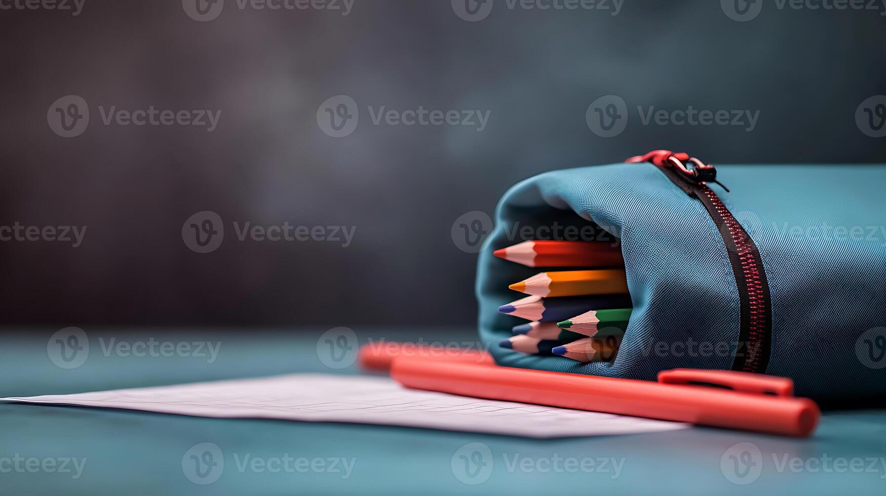 Colorful pencils spilling from a teal pencil case next to a red pen on a lined paper sheet photo