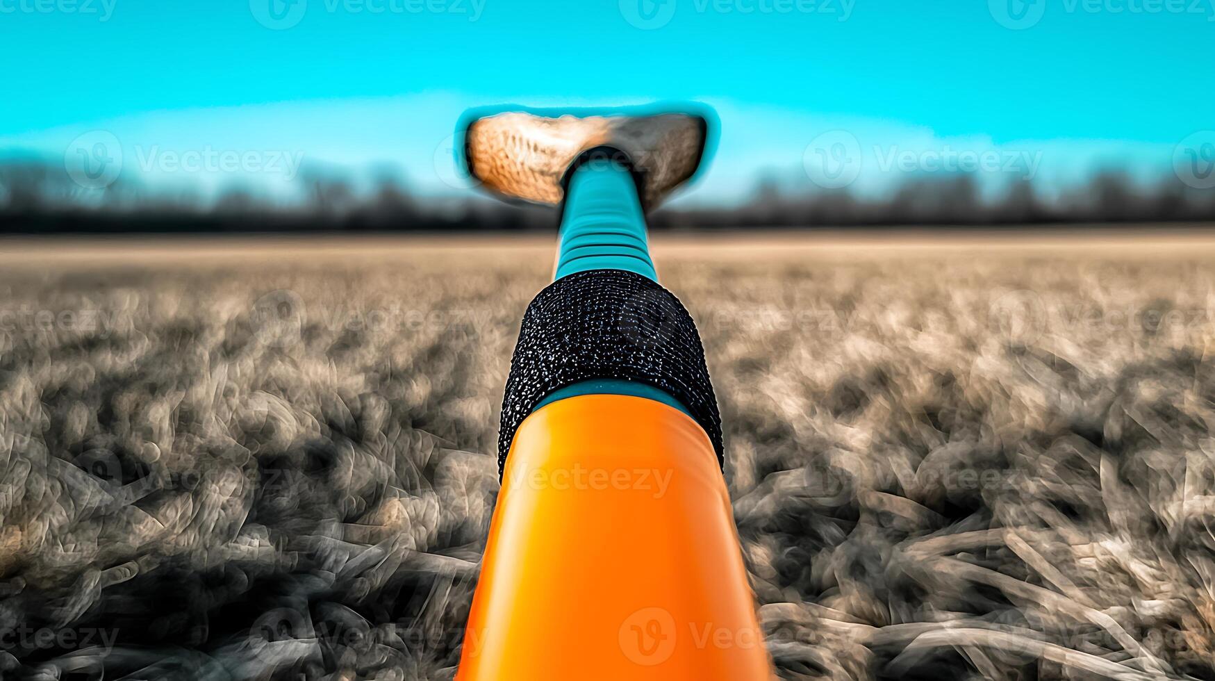 Close-up view of a vibrant orange sports bat resting on a grassy field under a clear blue sky photo