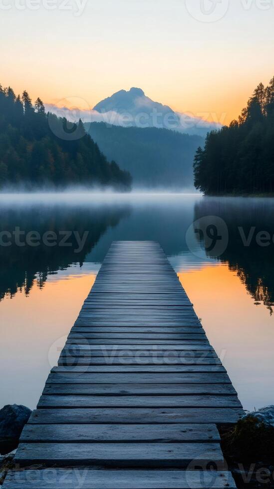 Wooden pier stretching into misty lake at sunrise with mountain view photo