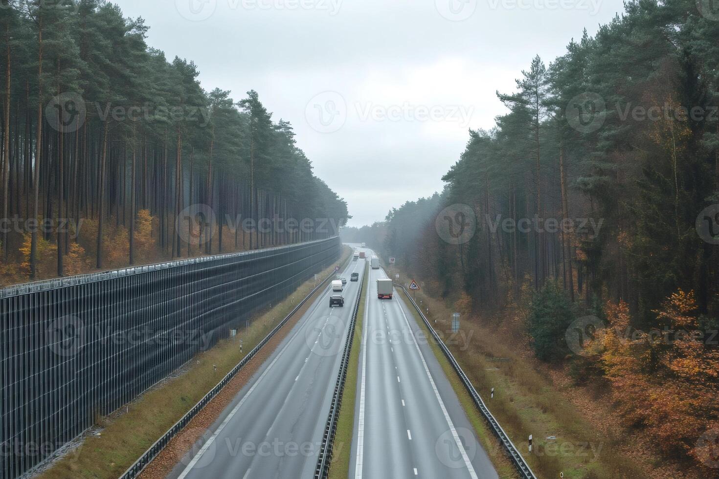 Highway traffic passing through a forest with soundproof wall on a rainy day photo