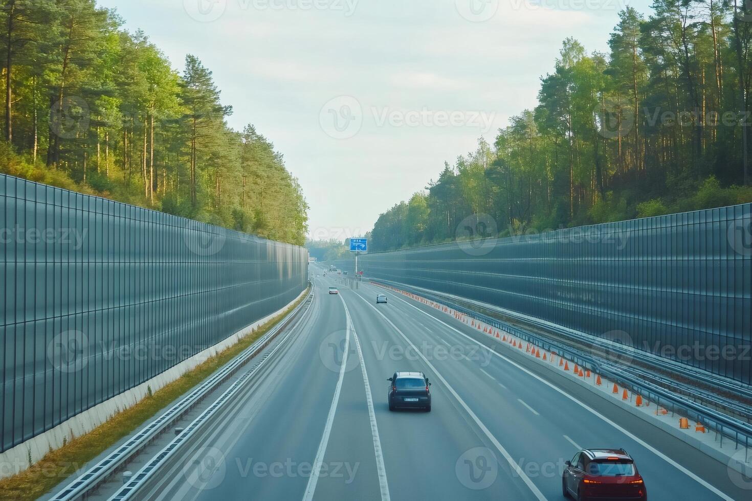 Cars driving on highway with noise barriers and forest in background photo