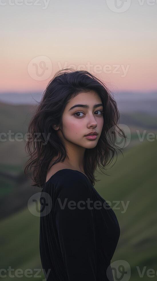 A woman with dark hair and dark eyes standing in front of a green field photo